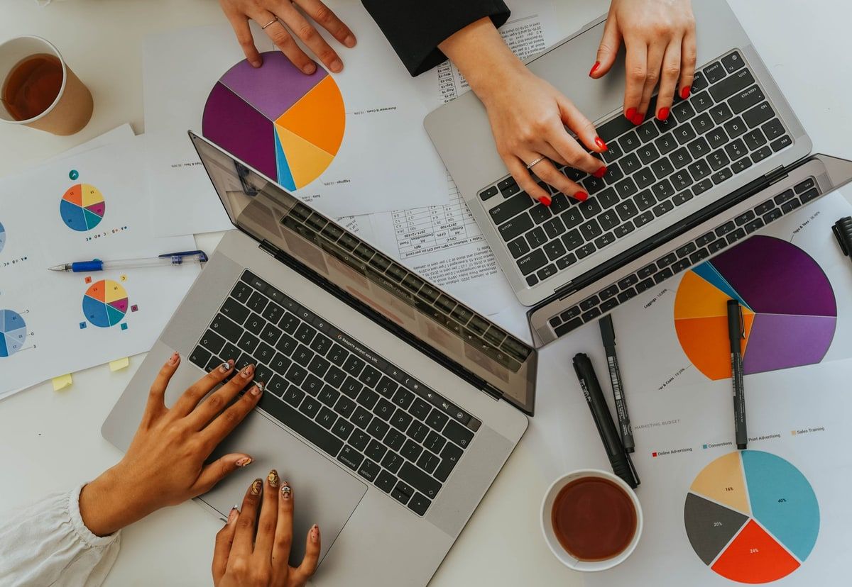 Overhead view of a team comparing colourful business charts beside three laptops