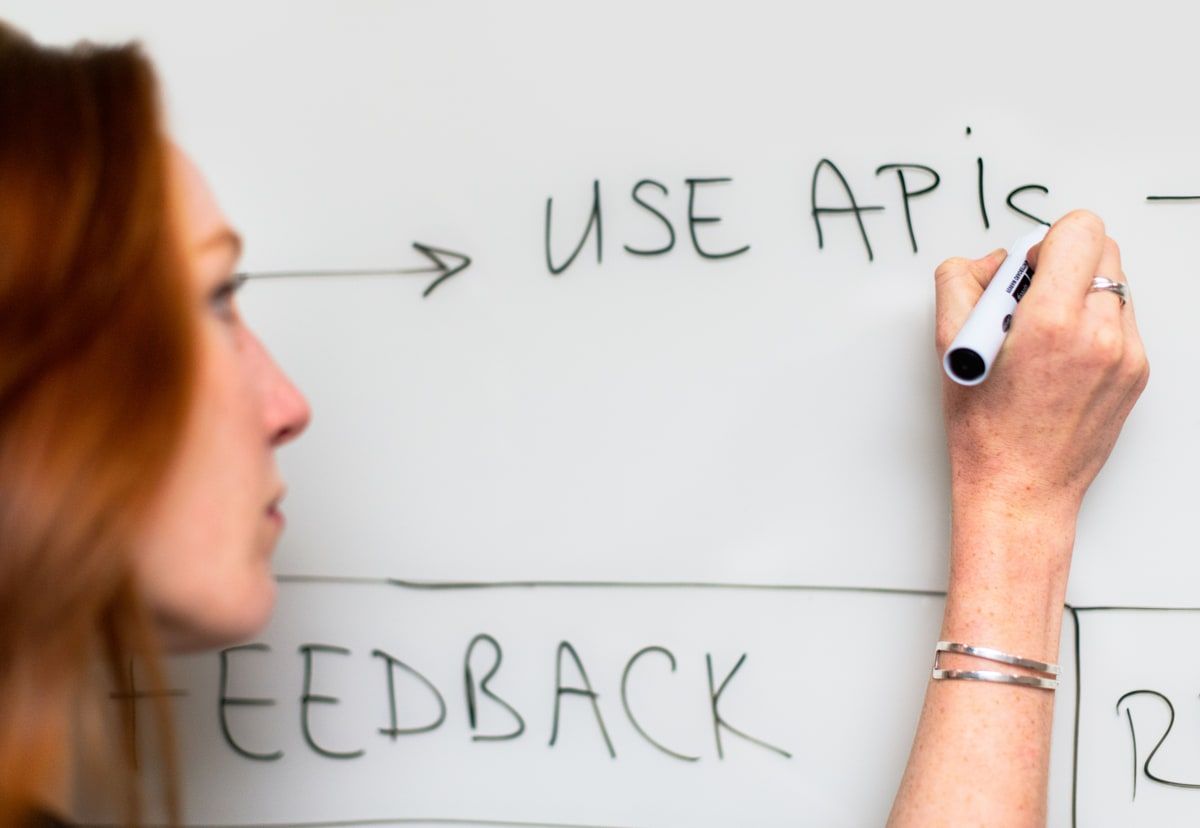 A software engineer writing Use APIs beside a flow diagram on a whiteboard