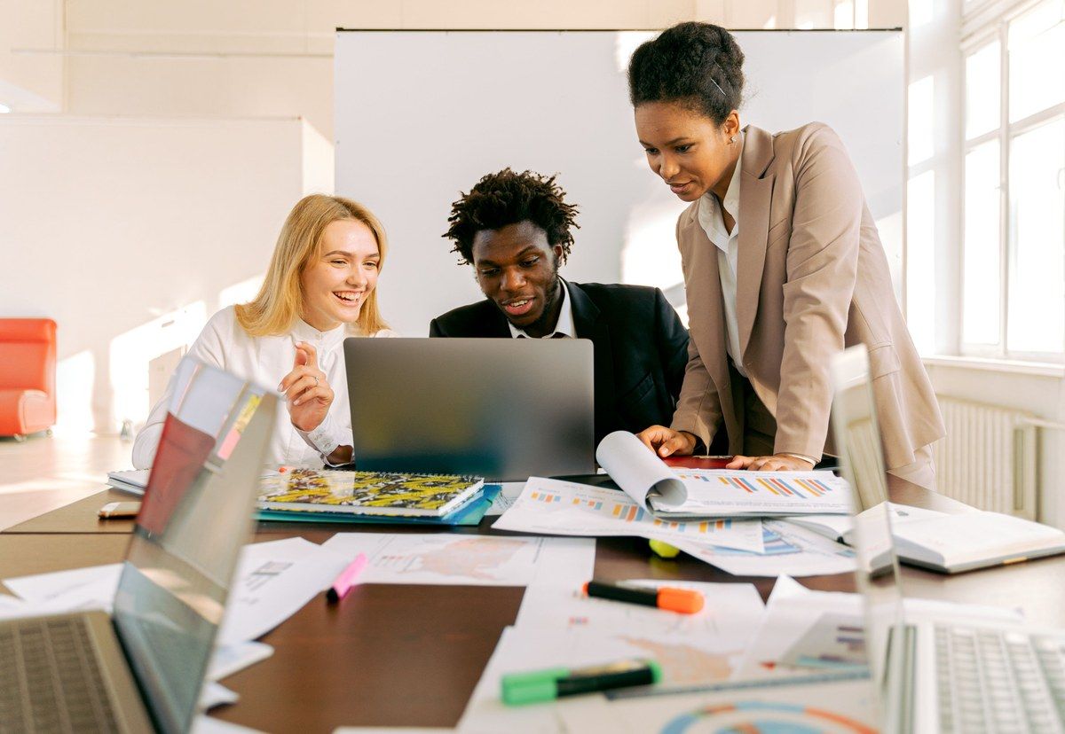 Three colleagues compare plans around a laptop in a bright office before making a technology decision.