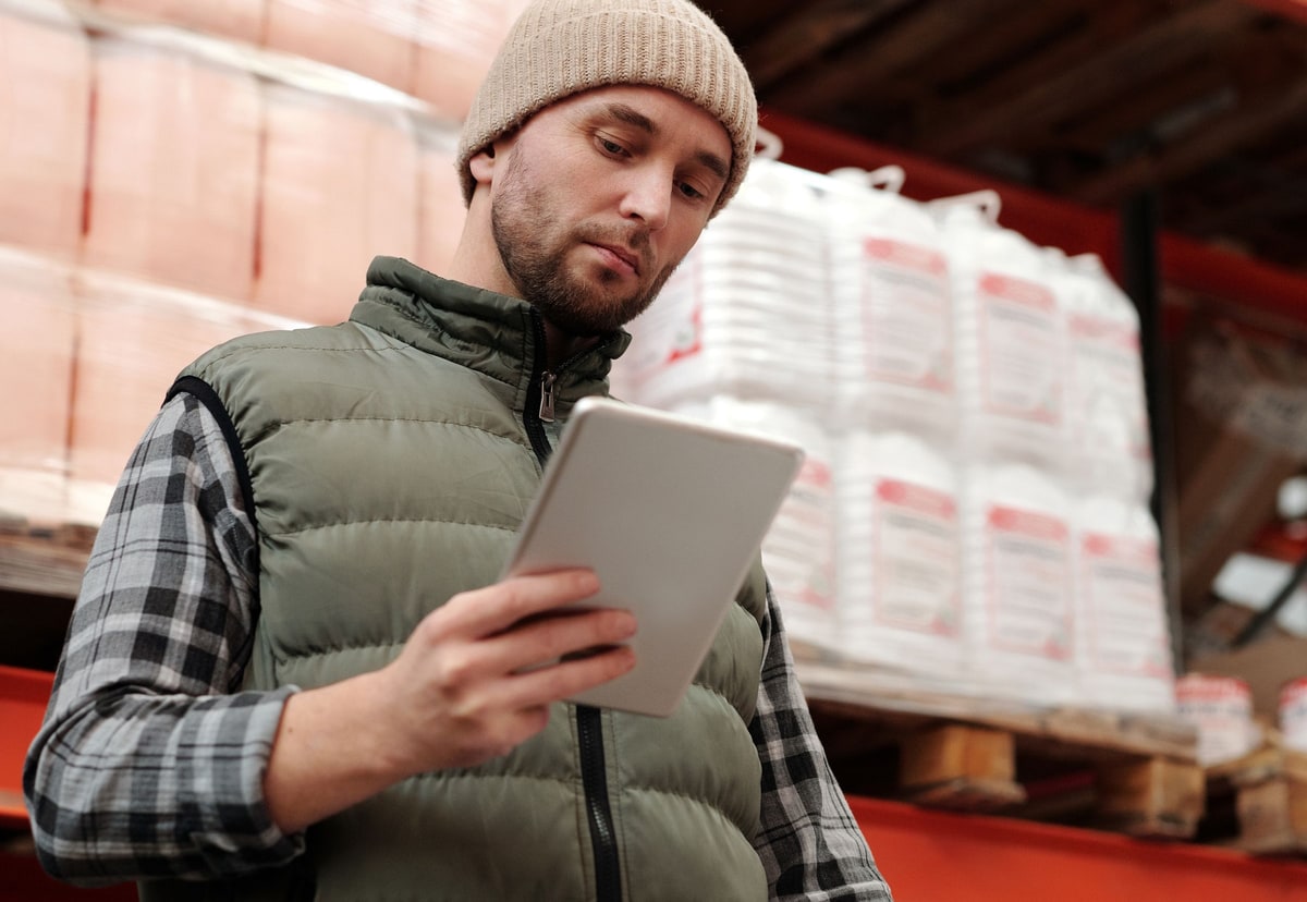 Warehouse worker reviewing inventory records on a tablet beside stored goods