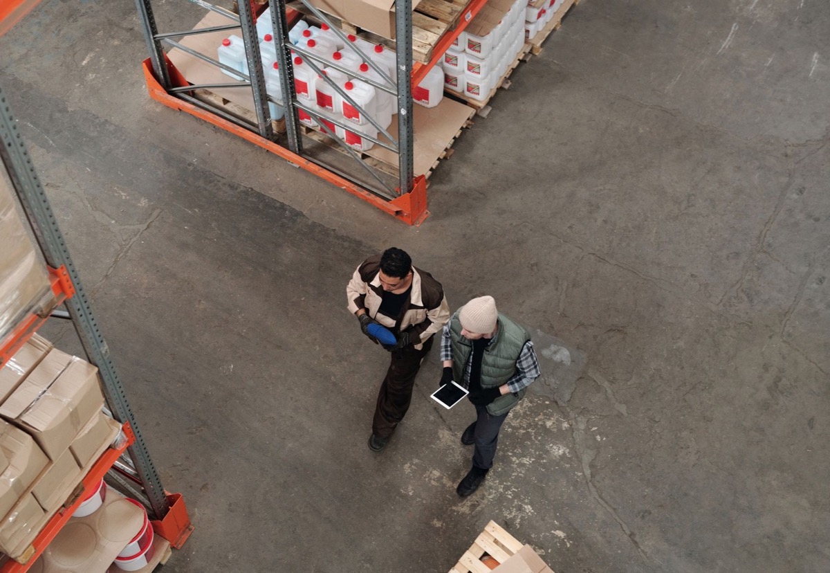 Two warehouse colleagues coordinating inventory work with a tablet between storage racks