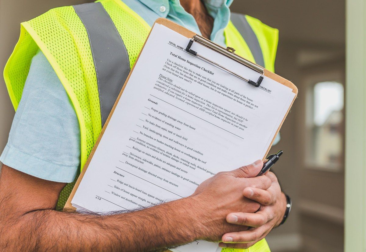 Home inspector in a high visibility vest holding a property inspection checklist on a clipboard.