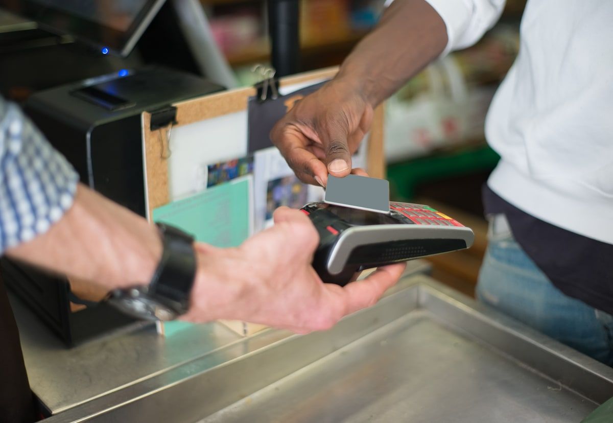A customer taps a payment card on a contactless card reader at a shop counter