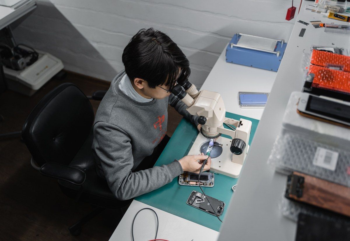 A technician examining an open smartphone with precision tools under a microscope