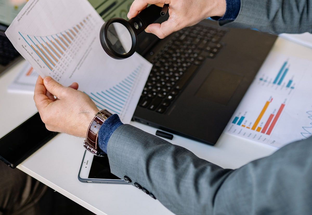 Business team examining printed charts with a magnifying glass beside a laptop