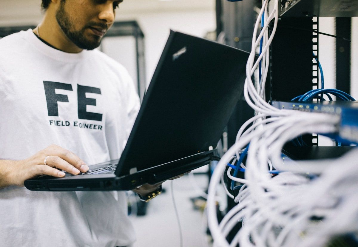 Field engineer using a laptop beside network equipment and cables in a server room