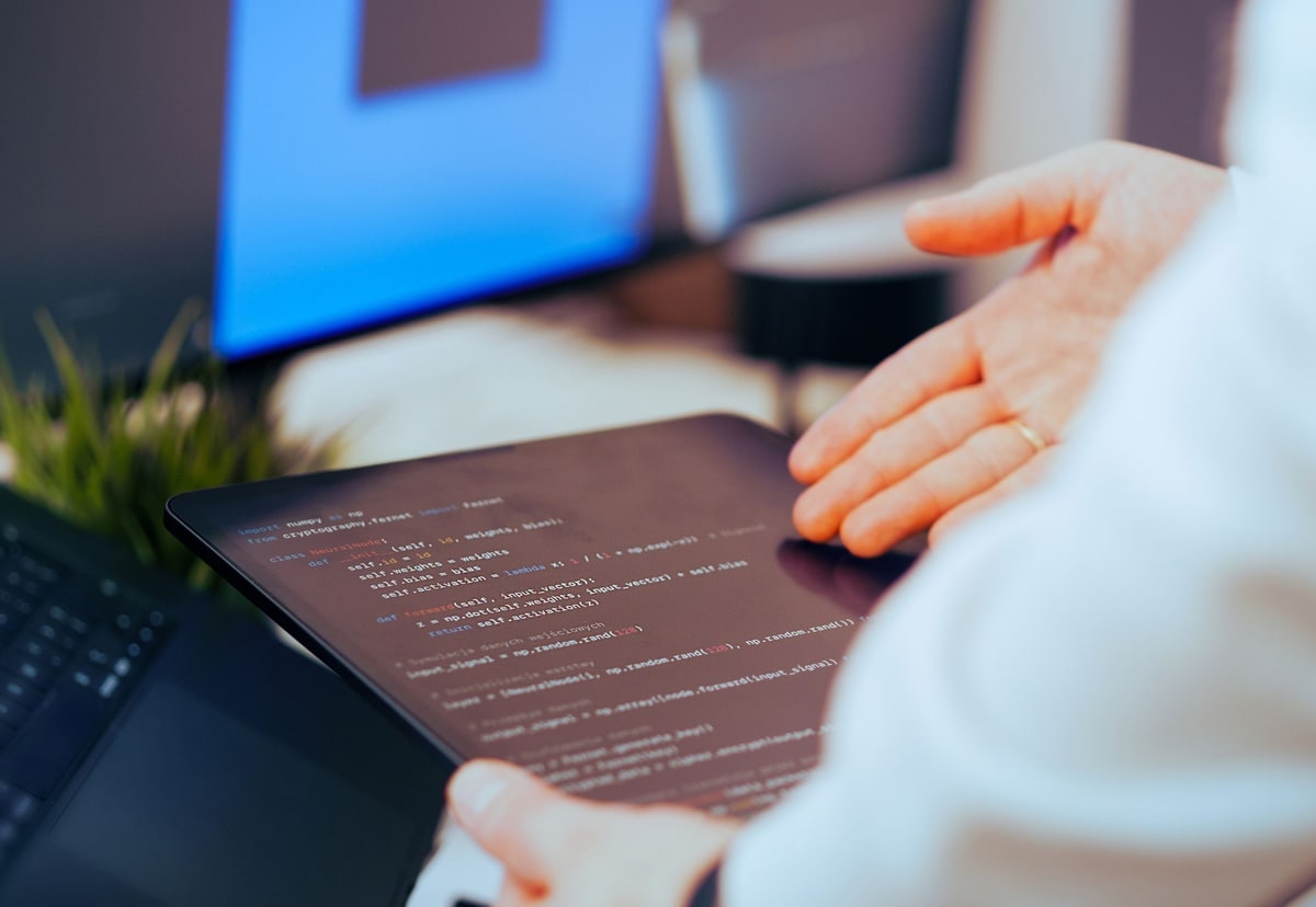 A developer reviewing code on a tablet beside a desktop monitor