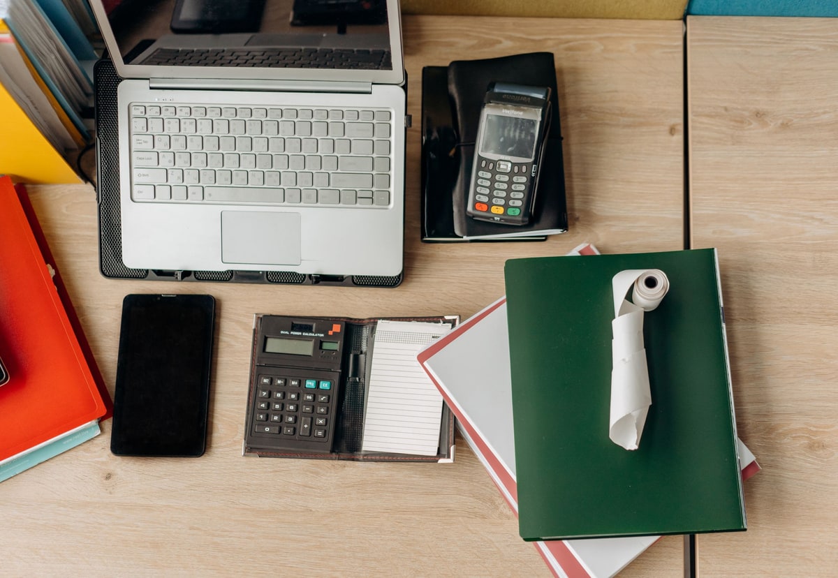Organised finance desk with a laptop, payment equipment, calculator and business records