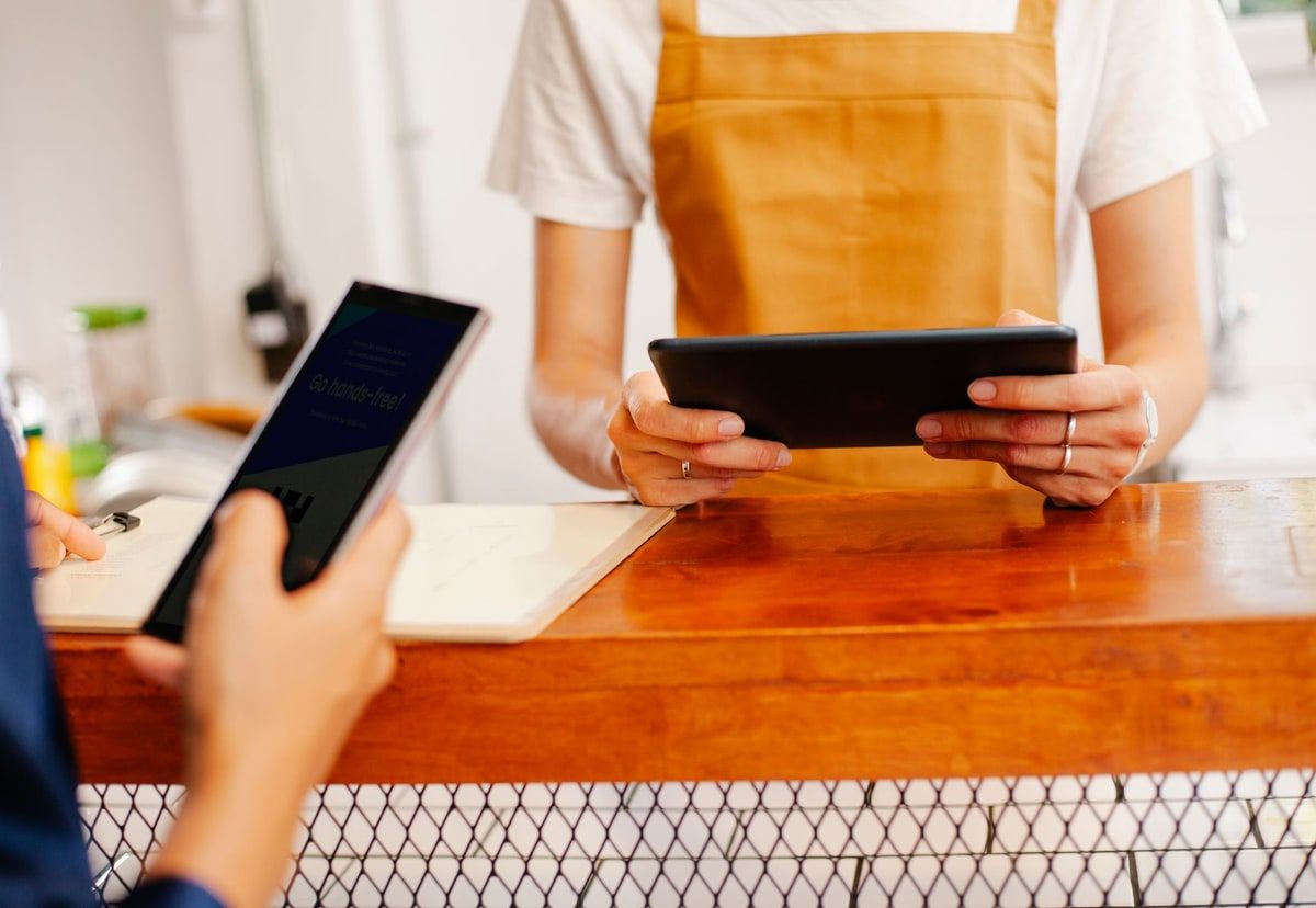 A cafe worker using a tablet while a customer holds a smartphone across the counter