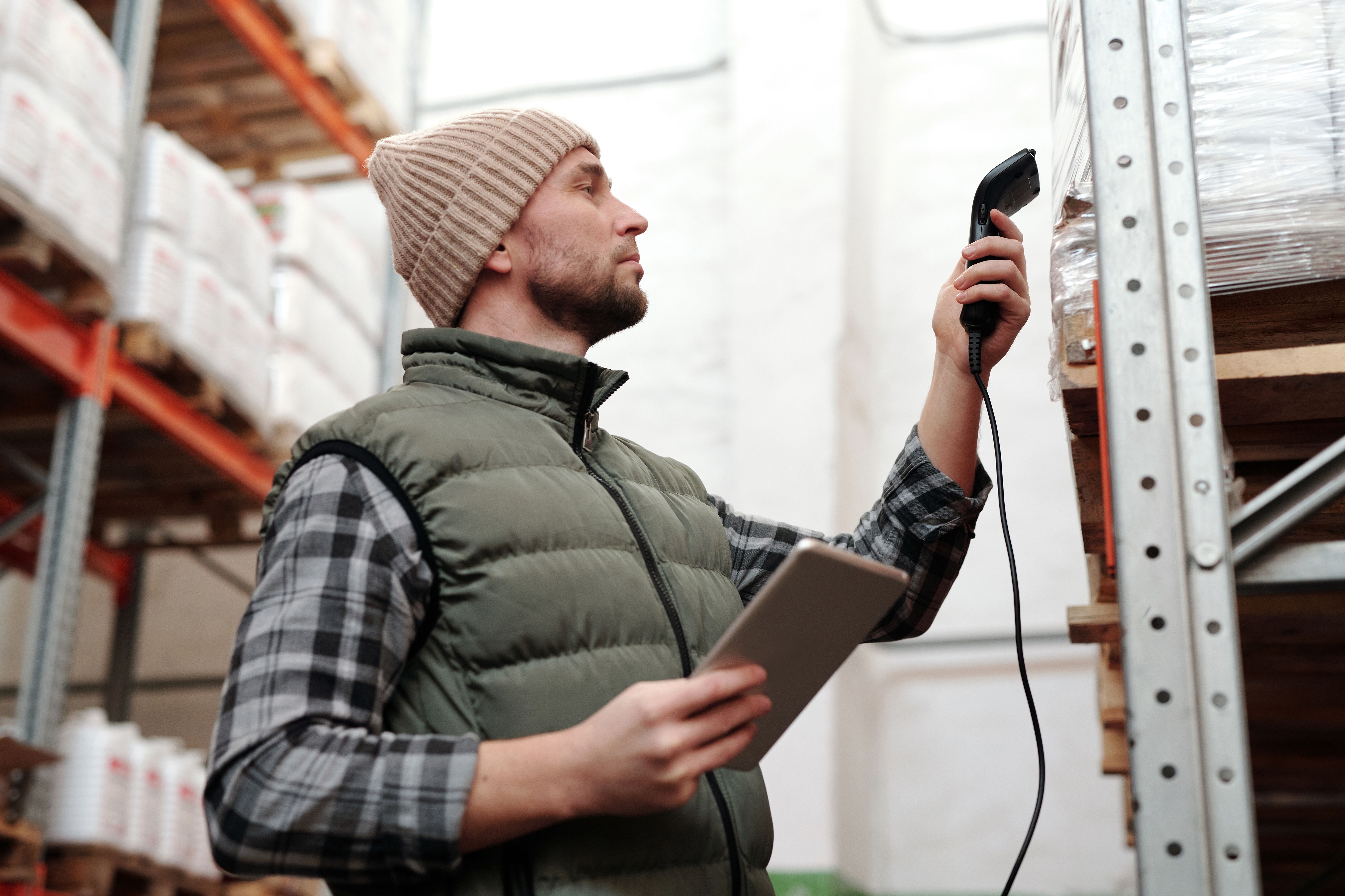 Warehouse employee scans inventory with a handheld barcode reader while holding a tablet, showing technology embedded in an everyday operational workflow