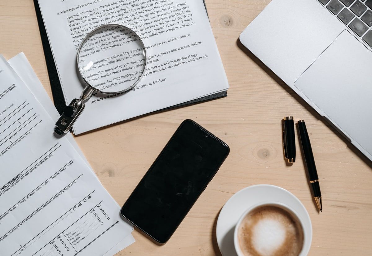 Natural-colour overhead view of documents, a magnifying glass, laptop and phone arranged for careful financial-services review