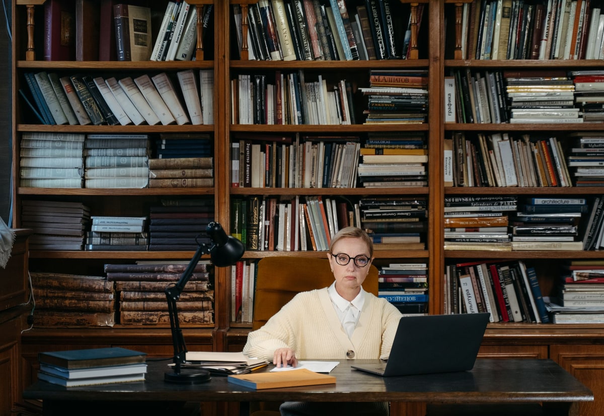 Professional working on a laptop at a desk in front of shelves filled with reference books