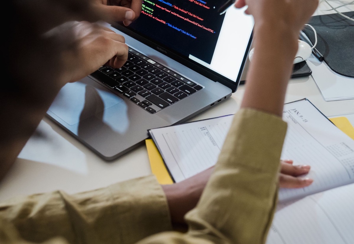 Two people reviewing code together on a laptop with a notebook beside them