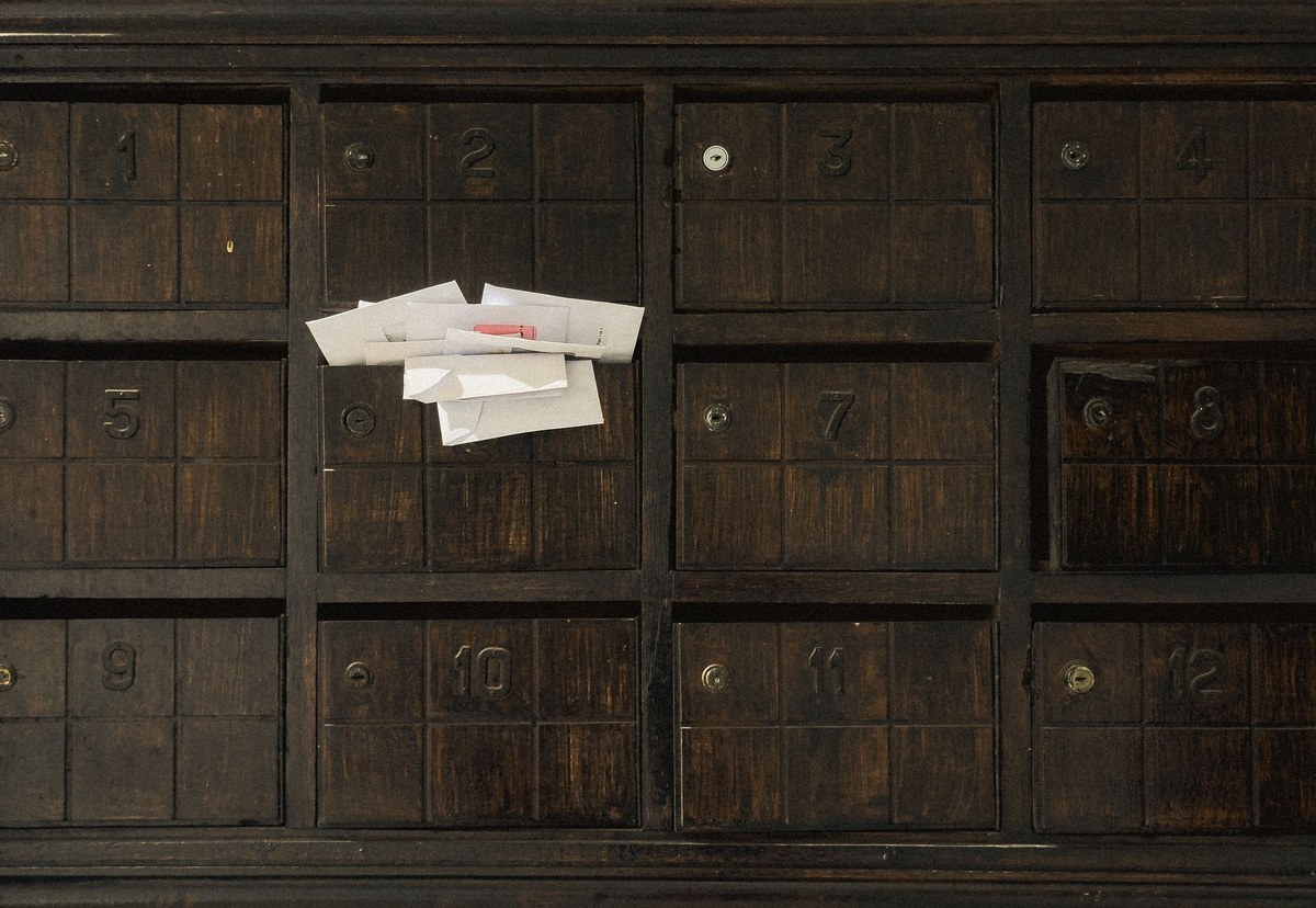 A wall of numbered wooden mailboxes with several white letters waiting in one slot