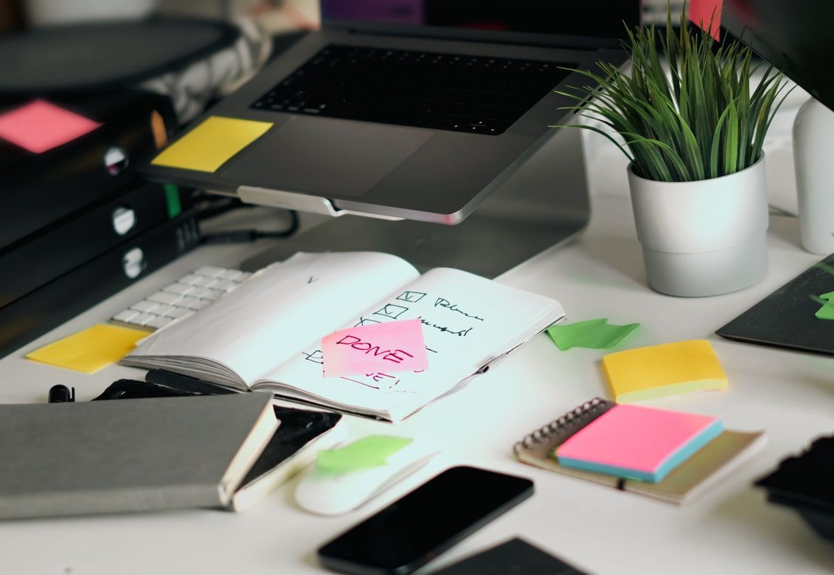 Organised desk with a laptop, notebook checklist and colourful sticky notes