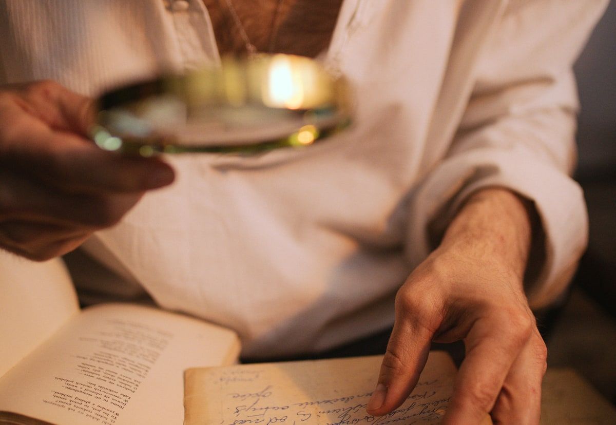 A person uses a magnifying glass to inspect handwritten documents, representing access to provider details behind a Laravel AI response