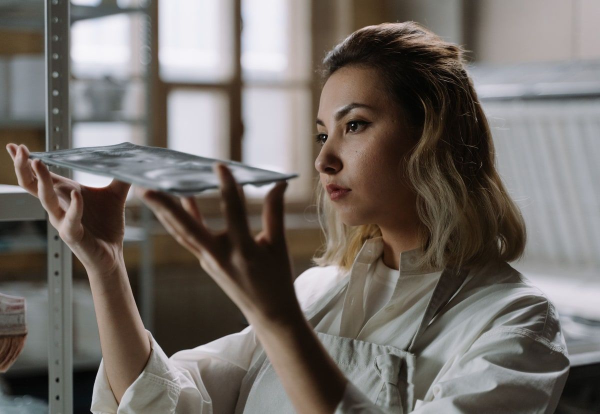 A craftsperson holds a sheet of glass up to the light to inspect its surface, representing careful review of AI-generated Laravel tests