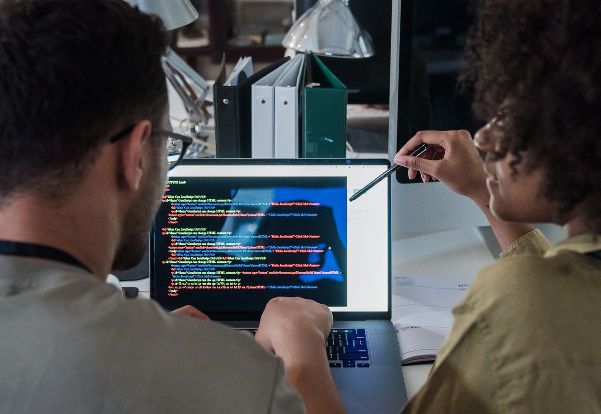 Two software developers reviewing application code together on a laptop in an office