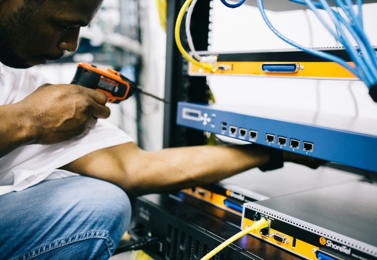 Engineer using a laptop beside server racks while checking application hosting infrastructure