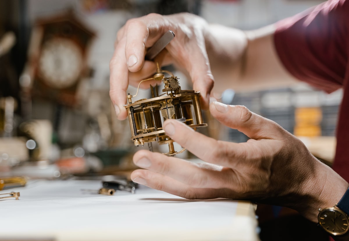 Hands carefully inspecting and repairing an old brass clock mechanism on a workshop bench