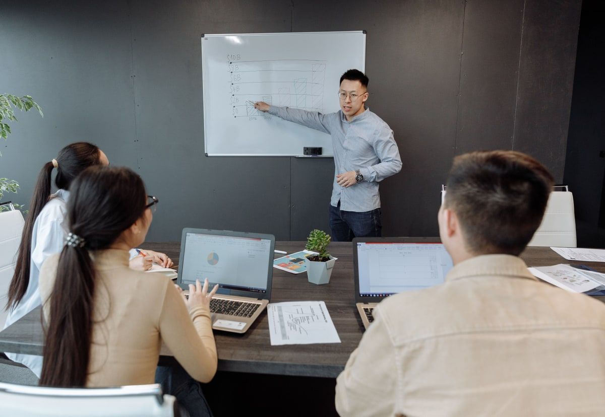 Startup team reviewing product plans around laptops and a whiteboard in a modern office