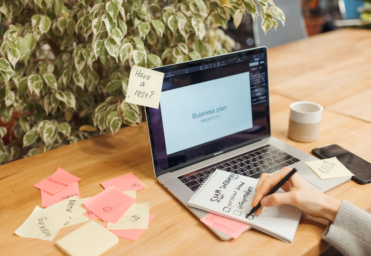 A person organising handwritten notes beside a laptop on a wooden desk