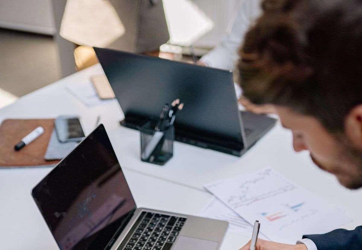 Business researcher taking notes beside a laptop and printed charts