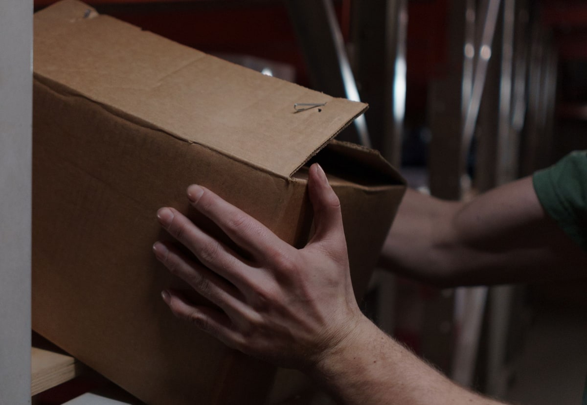A warehouse worker selecting a cardboard package from a storage shelf