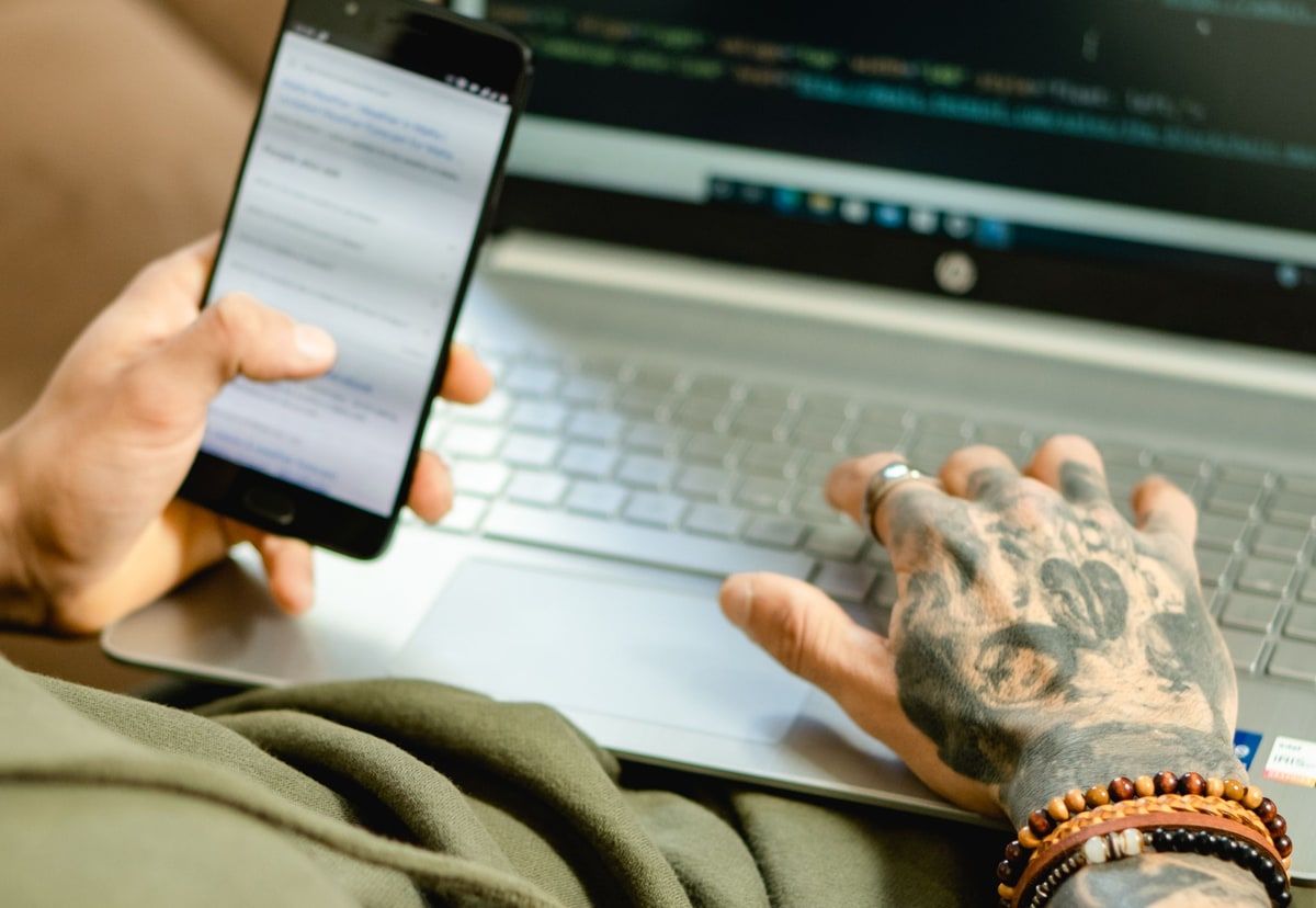 Developer checking a mobile page while working on application code on a laptop