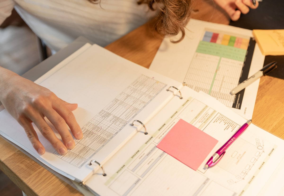 An employee working through a binder of forms and paperwork on a desk
