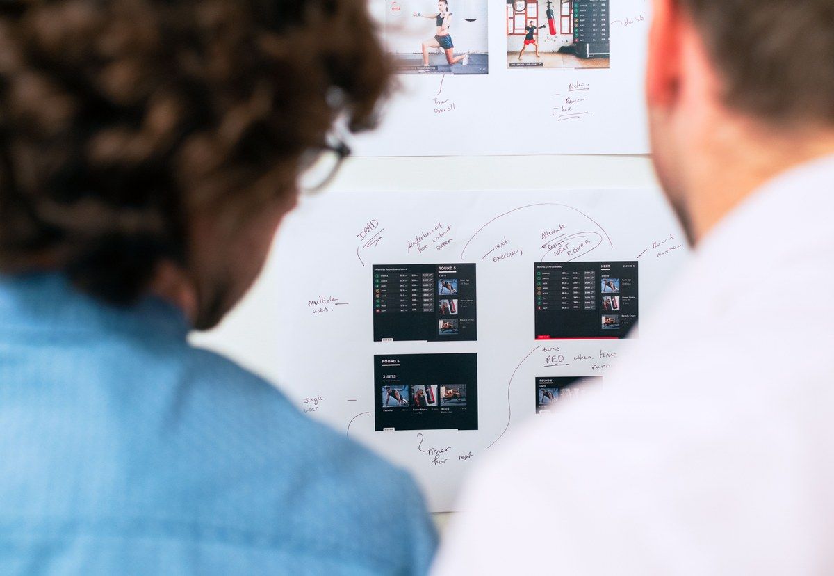 Two software professionals reviewing product screens and handwritten workflow notes on a whiteboard.