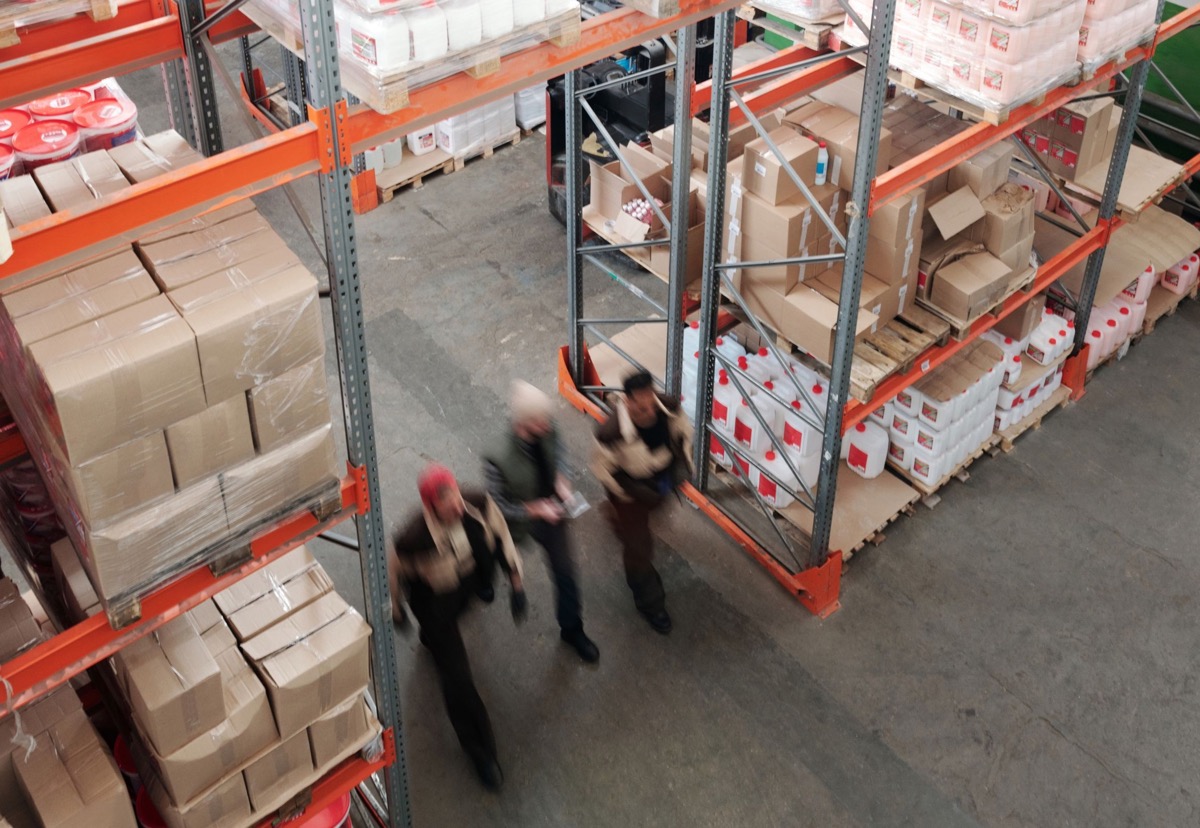 Workers moving through a large warehouse with organised racks and repeated rows of stock