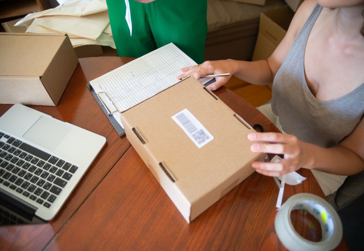 Two people packing online orders at a table beside a laptop and shipping boxes.