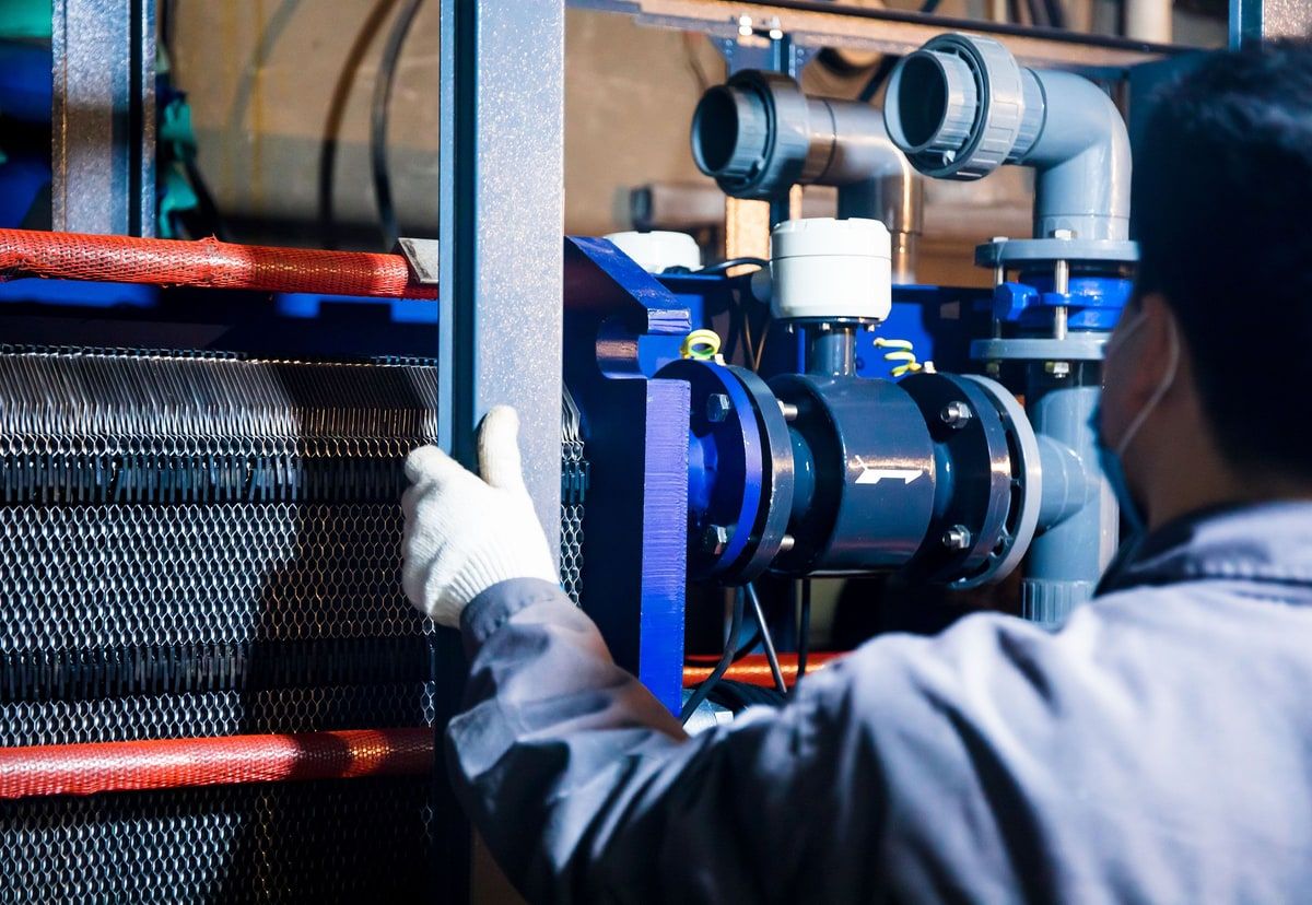 Natural-colour view of an engineer inspecting pipework and industrial machinery on a factory floor