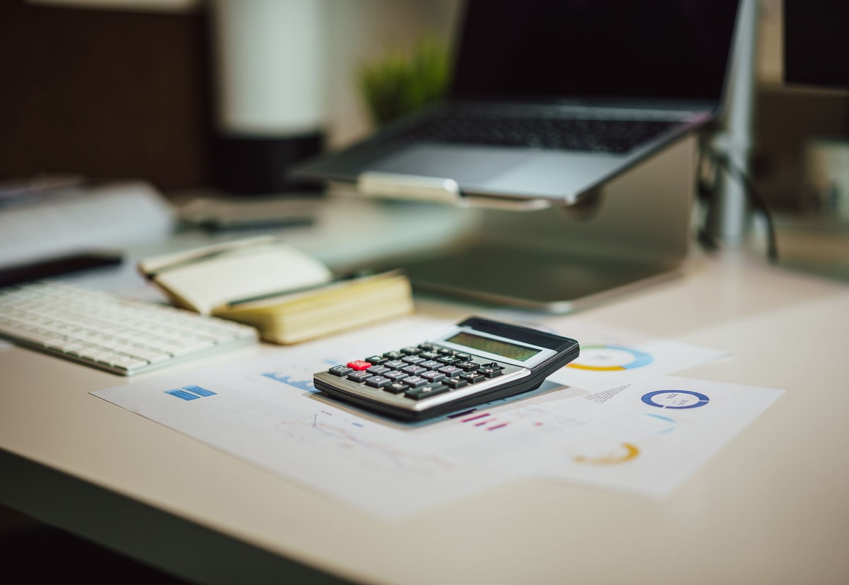 A calculator resting on printed business reports beside a laptop and notebook