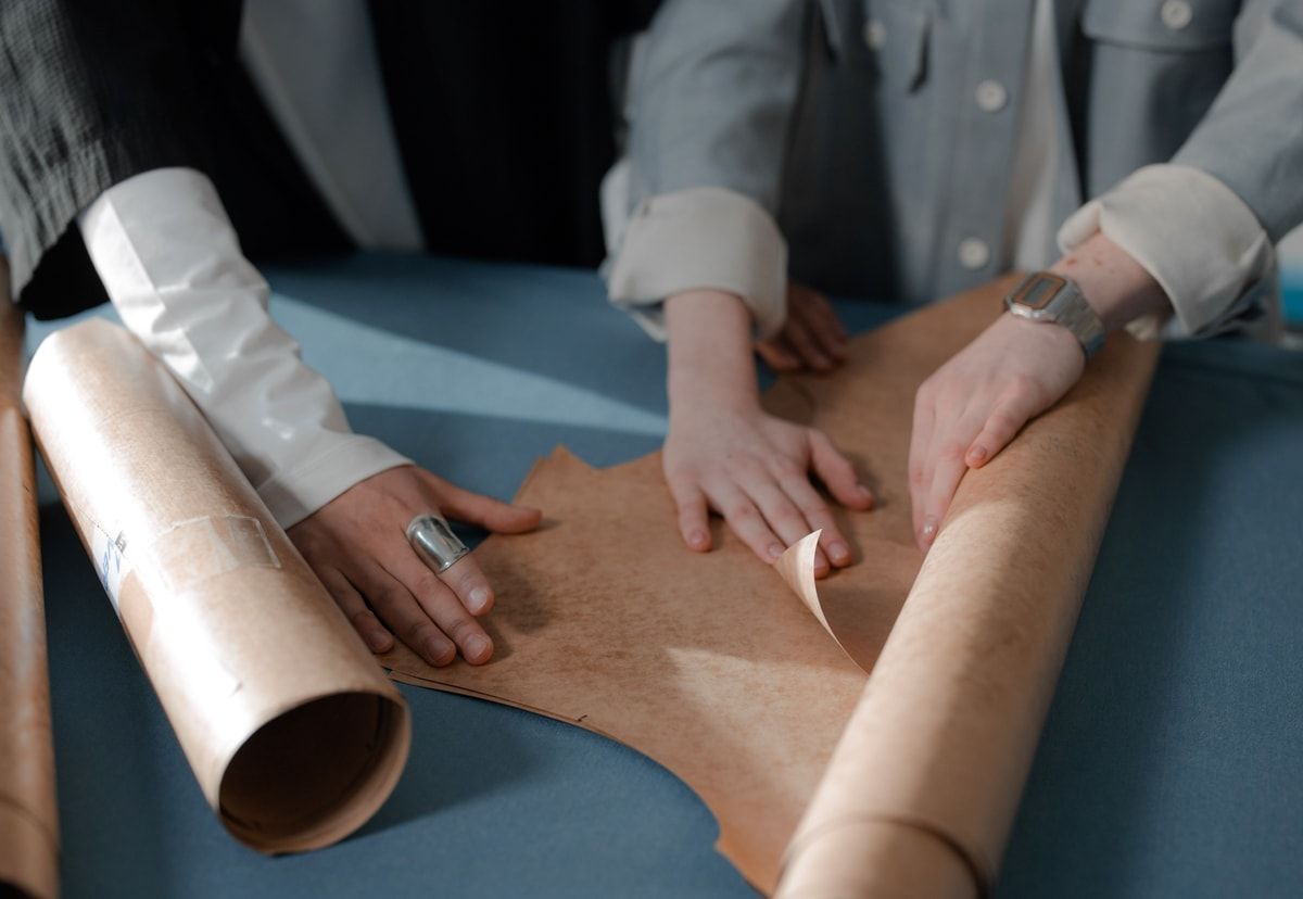 Three people arranging and marking brown paper design patterns together on a blue work surface