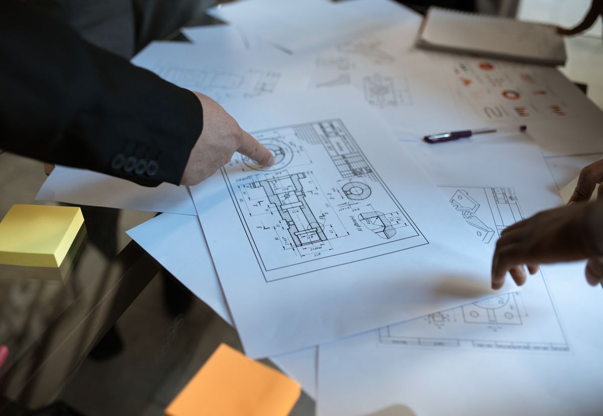 Two professionals pointing at detailed project plans spread across a desk during a risk review