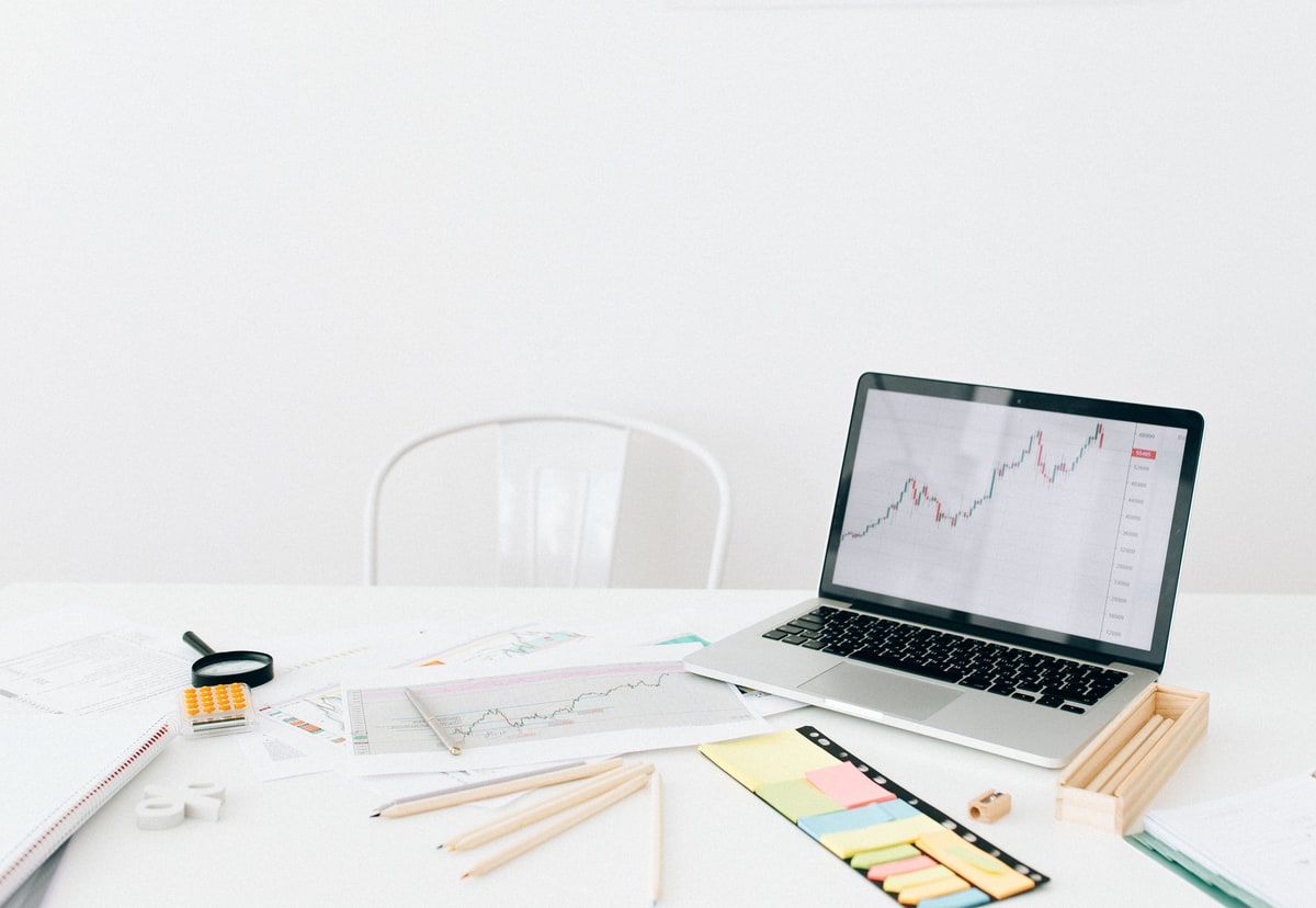 Natural-colour photograph of a laptop displaying charts beside printed reports and office stationery on a white desk