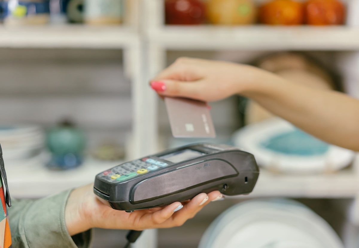 Customer holding a payment card above a handheld card terminal at a shop counter
