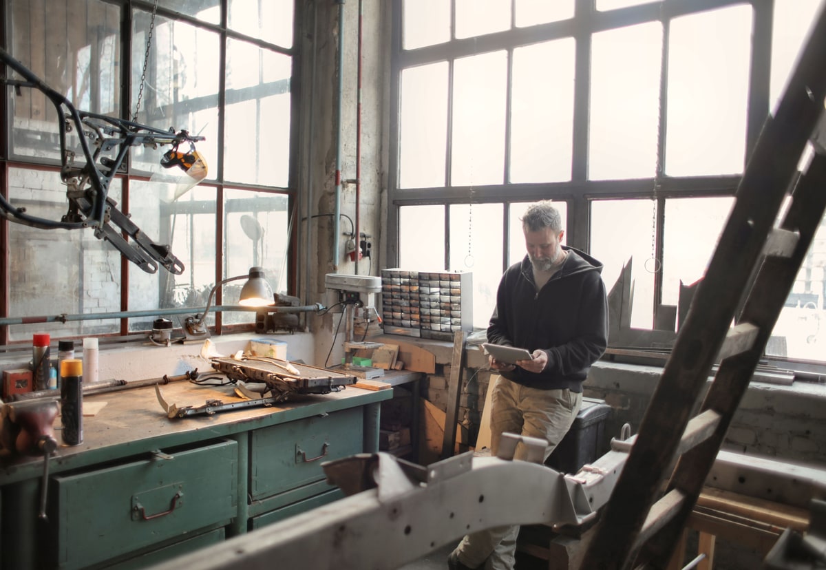 A technician checks a tablet beside machinery and tools in a working industrial workshop