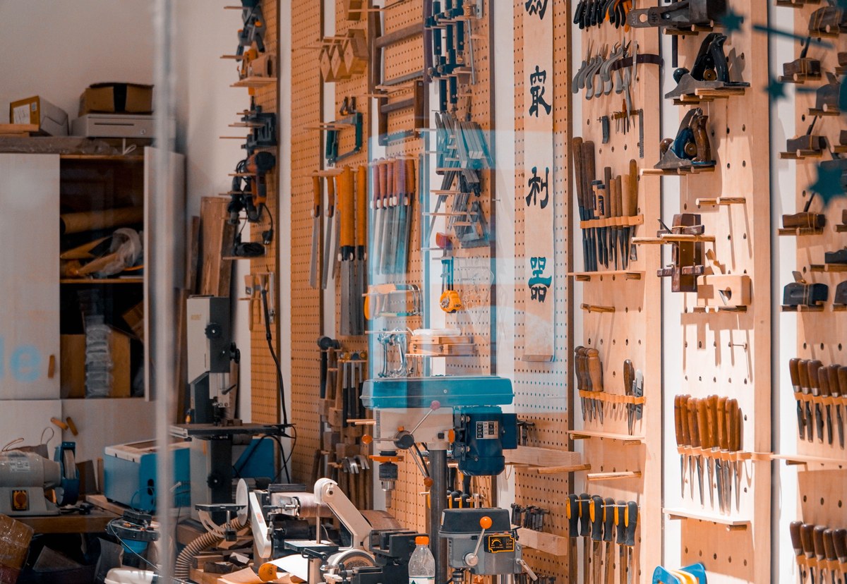 An organised woodworking workshop with hand tools arranged on a wooden wall above the machinery