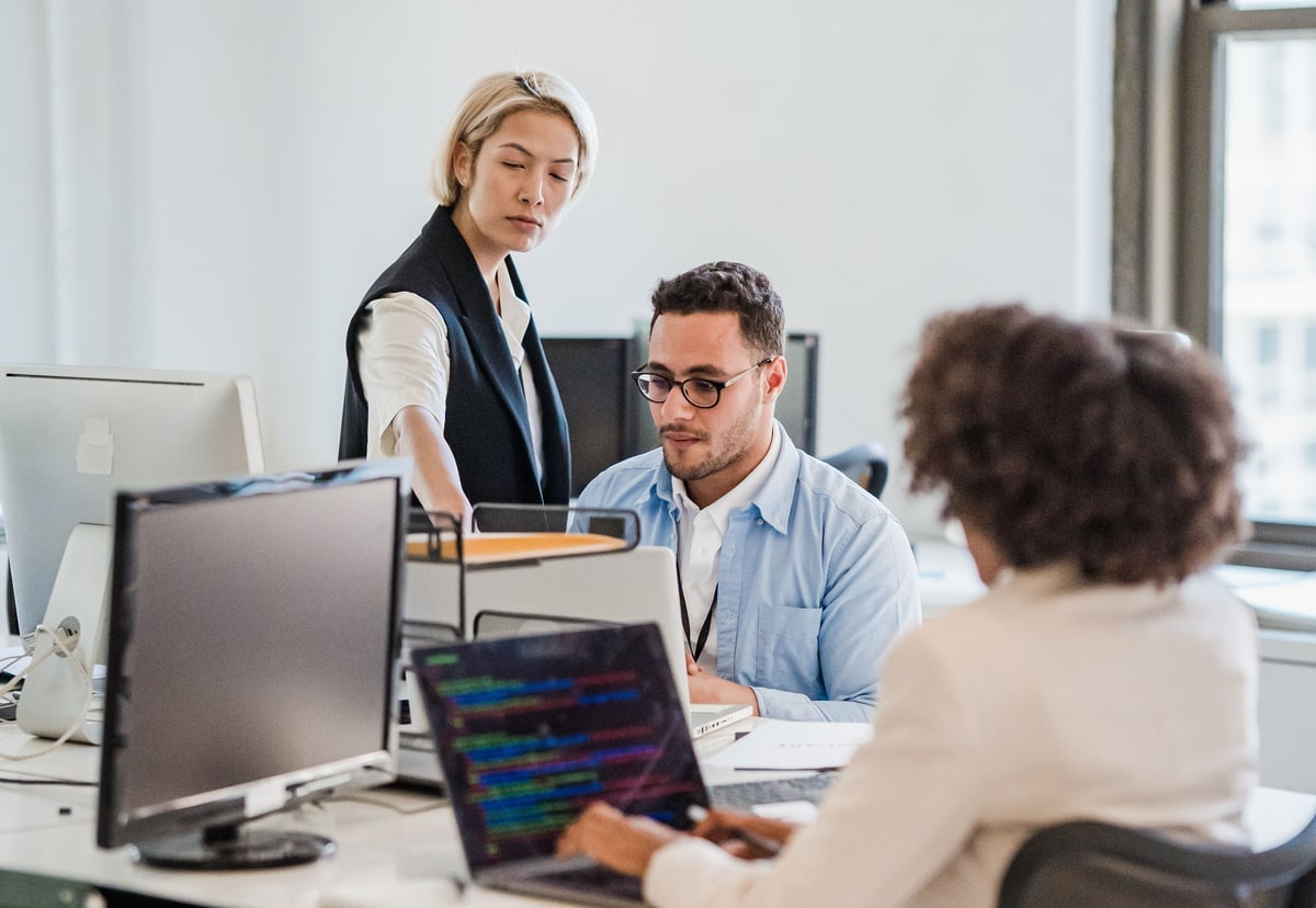 Three colleagues working across several computers in a bright office