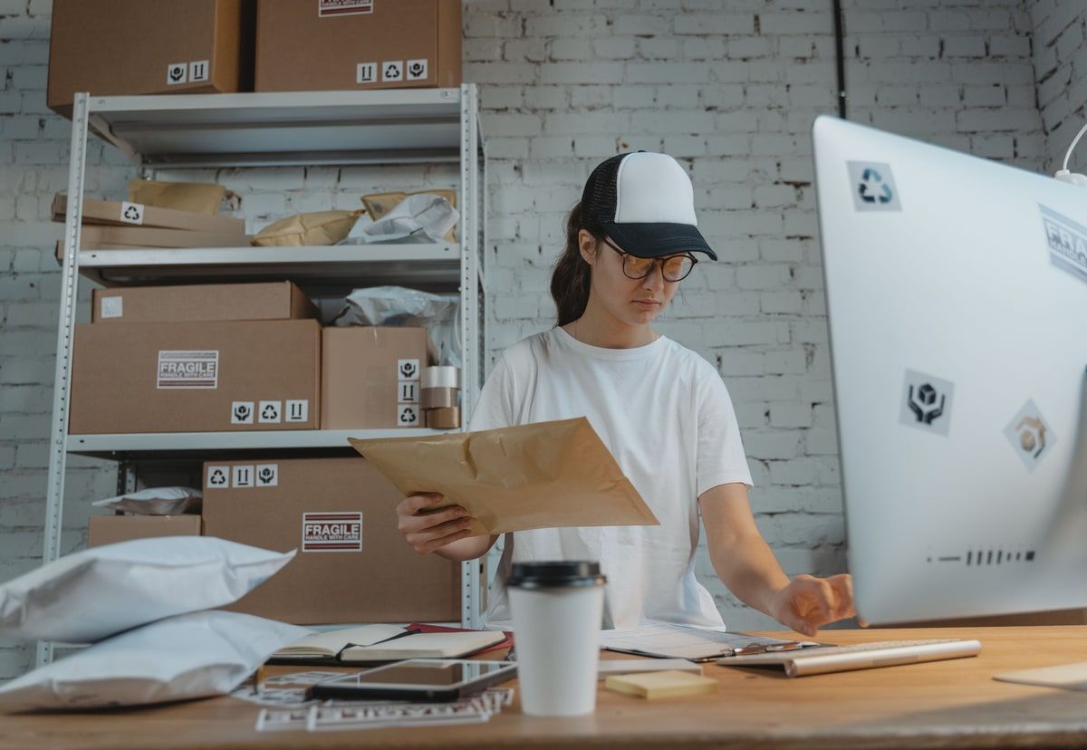 Warehouse worker checking paperwork beside labelled parcels and a computer