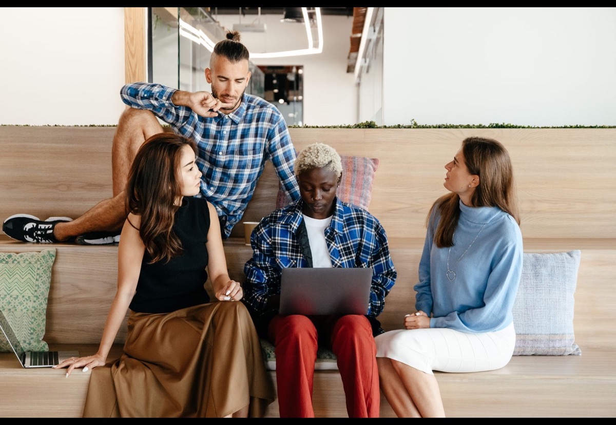 Four colleagues discussing customer work around a laptop in a bright office