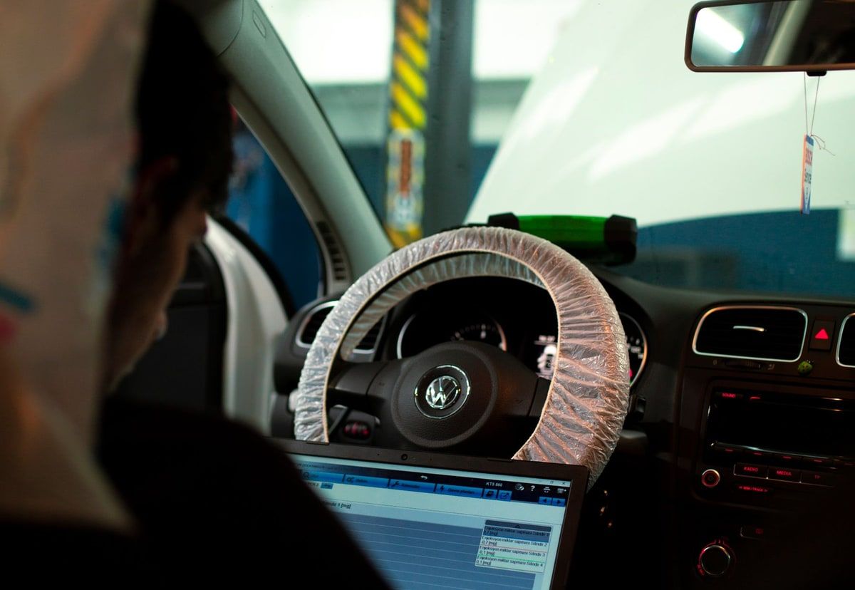 A vehicle technician using diagnostic software on a laptop inside a car